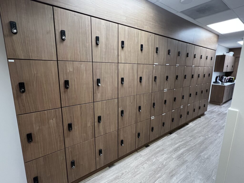 Modern locker room featuring rows of wooden lockers, equipped with combination locks, set in a bright, clean space with a speckled floor.