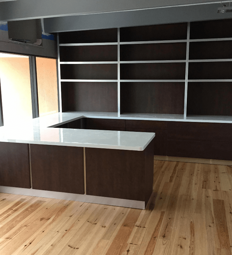 Modern kitchen space featuring a central island with a white countertop and dark cabinetry, complemented by open shelving and hardwood floors.